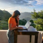woman in orange shirt sitting on white chair reading book
