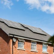 Brick house featuring solar panels on the roof under a clear blue sky, promoting sustainable energy.